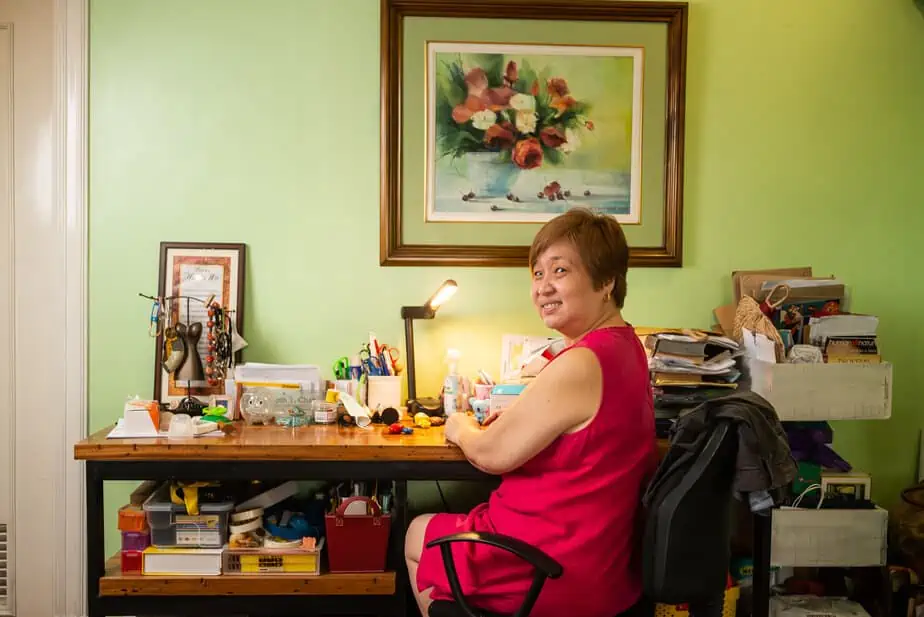 Lady in dark pink in front of wooden table with various office stuff.